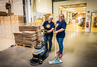 Das Bild zeigt zwei Mitarbeiterinnen, die in der Halle den Boden aufwischen, eine bedient eine Wischmaschine, eine hat einen Wischmopp.  | © SONNENTOR