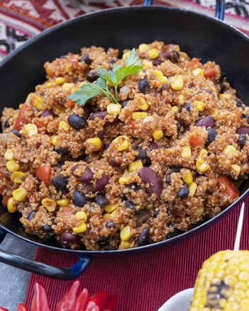 Auf dem Foto sieht man eine Pfanne mit veganem Quinoa Chili. Darauf ist frische Petersilie. Daneben sieht man einen Maiskolben. | © SONNENTOR